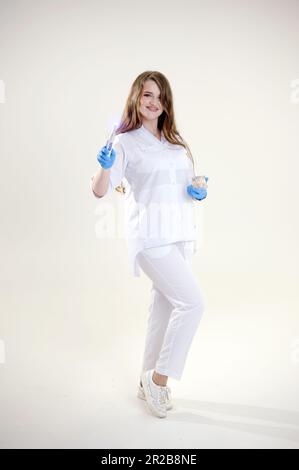 Fotopolimero lampada Dottor Fairy con una lampada blu brillante in un vestito medico bianco trattamento dentista dei denti protesi mettere otturazioni trattare gengive carie bella donna su sfondo bianco studio annuncio Foto Stock