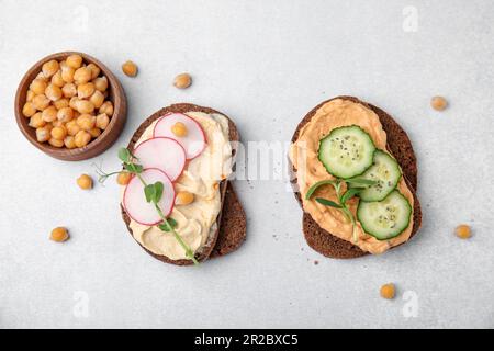 Deliziosi sandwich con hummus e diversi ingredienti su sfondo bianco, piatto Foto Stock