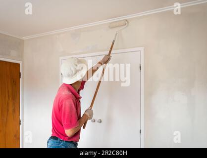 Uomo dipingendo pareti interne con un rullo. Progetto di ristrutturazione domestica. Auckland. Foto Stock