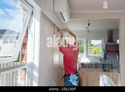 Uomo dipingere parete interna con un rullo in una casa residenziale. Progetto di ristrutturazione domestica. Auckland. Foto Stock