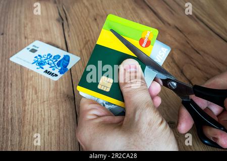 Aprile 2, 2022. Barnaul. Russia: Un uomo taglia le carte di credito bancarie del tipo e mastercard con le forbici. Distruzione delle carte di plastica dopo gli espirati Foto Stock