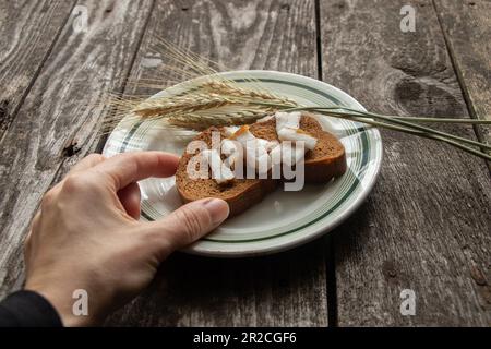 la mano femminile prende un pezzo di pane nero con aglio su un tavolo di legno per pranzo Foto Stock