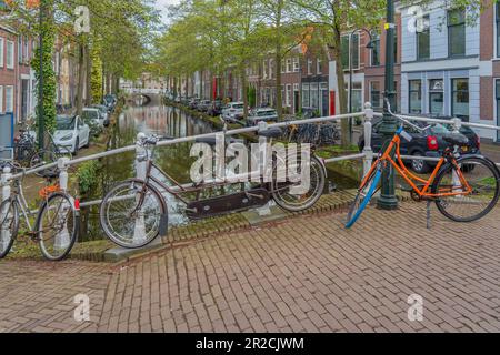 Delft, Paesi Bassi - 26 aprile 2023: Vecchio canale di Delft in primavera con bicicletta e gli edifici sul mare e alberi verdi Foto Stock