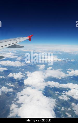 Una vista attraverso una finestra di un aereo durante il volo. Ala visibile, nuvole su terra e spazio. Trasporti aerei, trasporti e turismo. Foto Stock