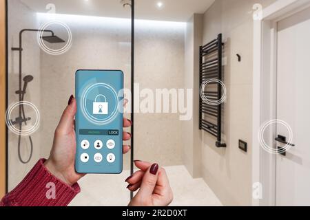 Primo piano smartphone in mano femminile con interfaccia app Smart Home System sullo schermo del cellulare, giovane donna che controlla tutto il sistema di casa tramite telefono Foto Stock