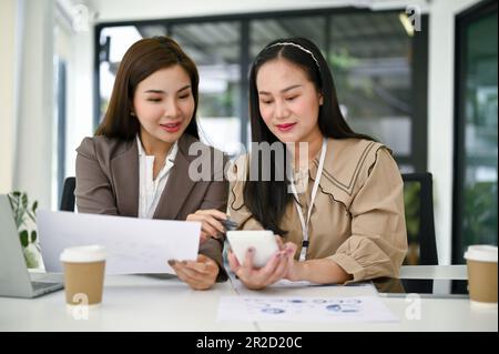 Le donne d'affari asiatiche o i ragionieri professionisti del millennio stanno lavorando, rivisitando i dati di vendite con calcolatore e analizzando i rapporti di dati finanziari dentro Foto Stock