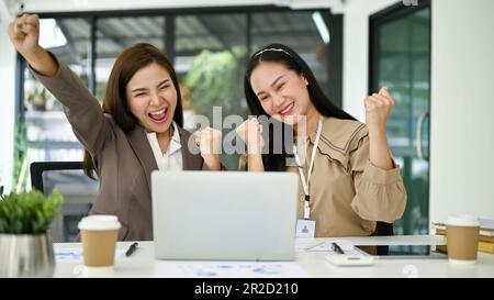 Due giovani imprenditrici asiatiche eccitate e gioite urlano di gioia, gioiscono e celebrano insieme il loro successo di progetto in ufficio. Foto Stock