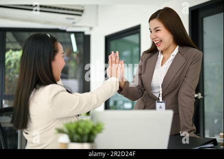 Due donne d'affari asiatiche allegre e gioiose stanno dando il massimo per celebrare il successo del loro progetto. Concetto di lavoro di squadra Foto Stock