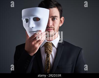 Ritratto a due facce, maschera e falso uomo d'affari in uno studio con faccia seria con personalità segreta. Manager e corporate maschio con cravatta in mostra Foto Stock