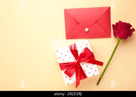 San Valentino: Busta rossa con lettera, regalo e rose rosse su sfondo beige. Vista dall'alto Foto Stock