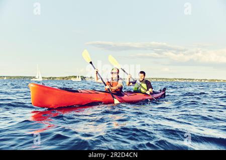 Giovane coppia in kayak tandem pagaia attraverso la baia di casco al tramonto Foto Stock