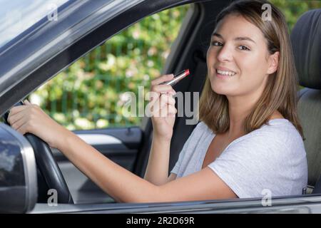 giovane donna di buon aspetto che applica rossetto in auto Foto Stock