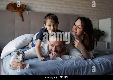 La famiglia è sdraiata sul letto comunicando via video sul telefono Foto Stock