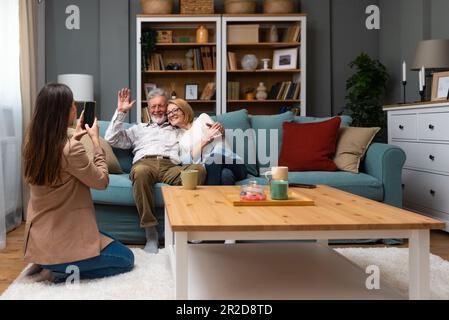 La figlia o la nipote che visitano i suoi genitori, una coppia anziana o i nonni scatta una foto di loro con il suo telefono e prende un selfie come memoria Foto Stock