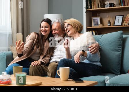 La figlia o la nipote che visitano i suoi genitori, una coppia anziana o i nonni scatta una foto di loro con il suo telefono e prende un selfie come memoria Foto Stock