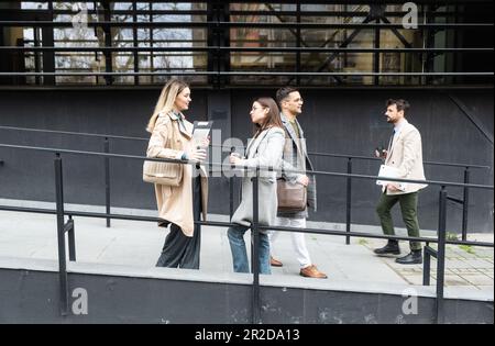 Una giornata normale per i lavoratori in piedi che parlano camminando davanti all'edificio degli uffici dove lavorano andando e uscendo dal luogo di lavoro. Uomini d'affari Foto Stock