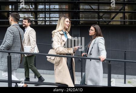 Una giornata normale per i lavoratori in piedi che parlano camminando davanti all'edificio degli uffici dove lavorano andando e uscendo dal luogo di lavoro. Uomini d'affari Foto Stock