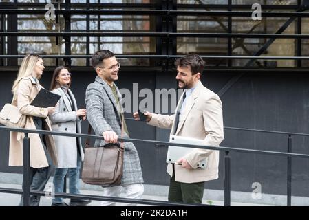 Una giornata normale per i lavoratori in piedi che parlano camminando davanti all'edificio degli uffici dove lavorano andando e uscendo dal luogo di lavoro. Uomini d'affari Foto Stock