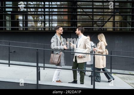 Una giornata normale per i lavoratori in piedi che parlano camminando davanti all'edificio degli uffici dove lavorano andando e uscendo dal luogo di lavoro. Uomini d'affari Foto Stock