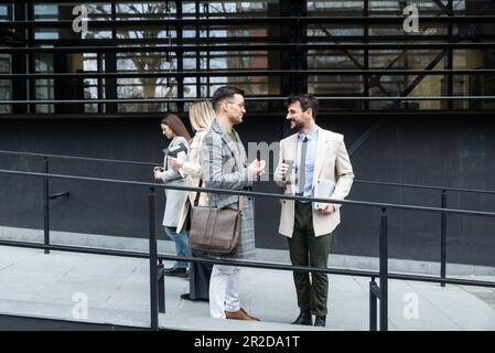 Breve briefing prima della riunione. Gruppo di giovani uomini d'affari allegri e di successo che parlano tra loro mentre camminano all'aperto. Esperti di impiegati Foto Stock