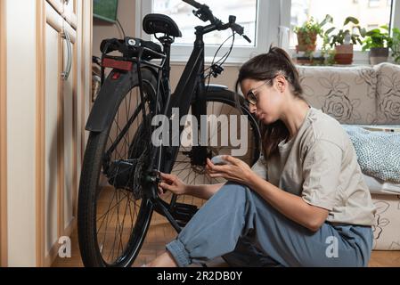 Giovane auto imparò donna o ragazza meccanico che fissa e ripara la sua bicicletta a casa sua. Catena di riparazione femmina sulla ruota posteriore prima di iniziare a guidare Foto Stock