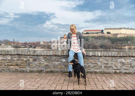 Ragazza giovane che cammina con il suo cane adottato fuori che ha salvato da un rifugio animale e bere caffè da asporto, insieme godere di un buon tempo Foto Stock