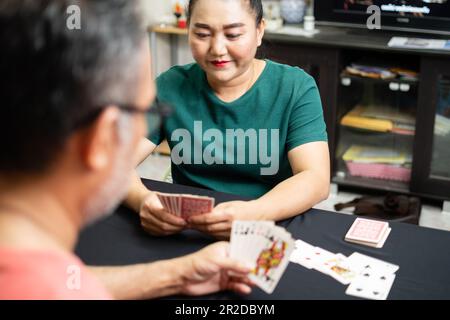 Coppie che giocano a carte a casa per la data notte all'interno. Entrambi tenevano le carte nelle loro mani e sorridevano felicemente. Il concetto per un gioco su, amore, godere, h Foto Stock