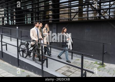 Gruppo di persone in viaggio d'affari che camminano all'esterno di fronte agli edifici degli uffici. Colleghi di successo che parlano di nuovi progetti di promozione del loro lavoro e autobus Foto Stock