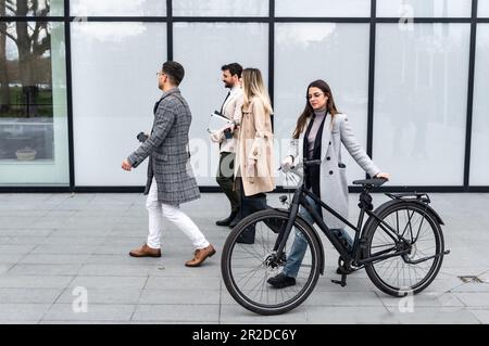 Gruppo di persone in viaggio d'affari che camminano all'esterno di fronte agli edifici degli uffici. Colleghi di successo che parlano di nuovi progetti di promozione del loro lavoro e autobus Foto Stock