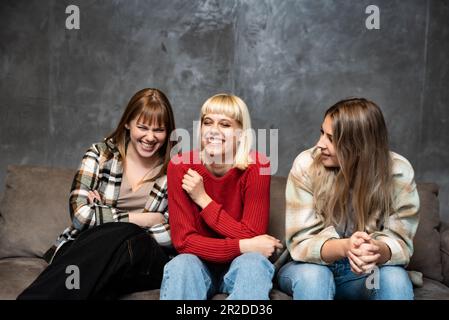 Tre giovani amici femminili, compagni di stanza del college sono seduti sul divano e ridendo perché sono felici e riusciti nelle loro vite. Foto Stock