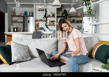 Felice giovane donna consumatore che tiene la carta di credito e il laptop che acquista online a casa. Cliente acquirente femmina che acquista sul mercato di Web site del ecommerce mak Foto Stock