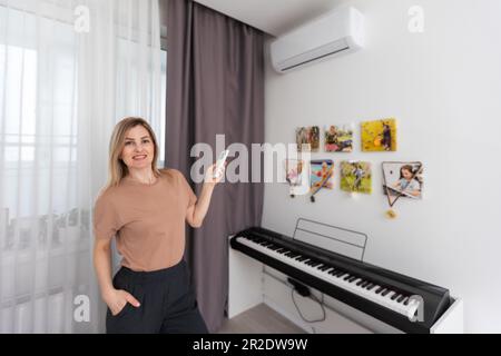 Donna che tiene il telecomando rivolto al condizionatore d'aria Foto Stock