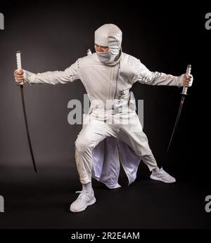 Ninja posa per una foto su uno sfondo nero, un ninja maschio in un kimono bianco Foto Stock