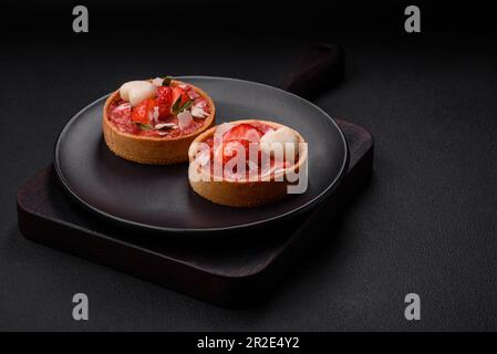 Deliziose tartine dolci fresche con fragole e fiocchi di cocco su fondo di cemento scuro Foto Stock