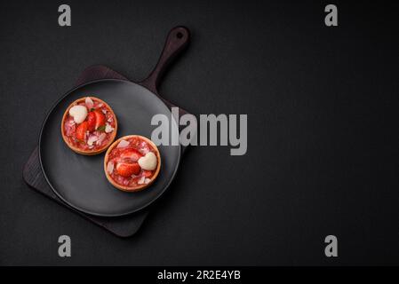 Deliziose tartine dolci fresche con fragole e fiocchi di cocco su fondo di cemento scuro Foto Stock