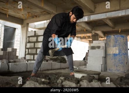 Un lavoratore che mescola manualmente cemento con una spata. Foto Stock