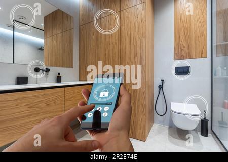 Primo piano smartphone in mano femminile con interfaccia app Smart Home System sullo schermo del cellulare, giovane donna che controlla tutto il sistema di casa tramite telefono Foto Stock