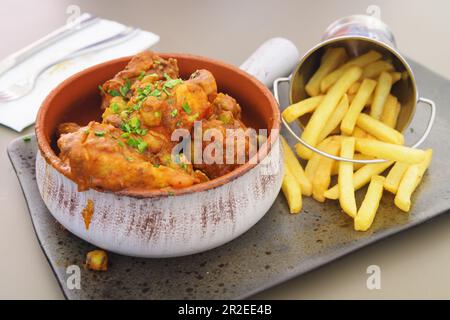 Stufato di coniglio saporito e piccante in salsa di pomodoro con patatine fritte come contorno in una disposizione piacevolmente placcata. Cucina tradizionale, gourmet e culinaria concep Foto Stock