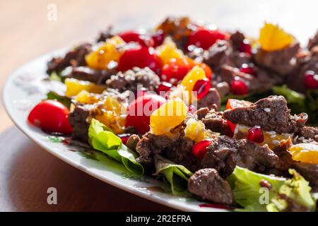 Foto ravvicinata dell'insalata calda con fegato di pollo, pomodori ciliegini, arancia, lattuga, semi di melograno e sesamo Foto Stock