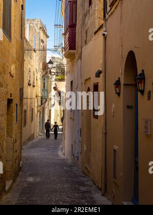 Rabat, Gozo, Malta - 18 aprile 2023: Una coppia a piedi in una strada stretta con architettura storica. Foto Stock