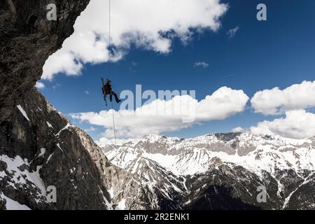 Alpinista si aggrappa su una parete rocciosa a strapiombo con uno sci sullo zaino, catena Mieminger, Tirolo, Austria Foto Stock