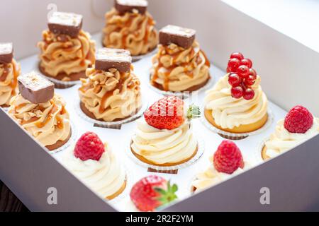 Set di diversi deliziosi cupcake con frutti di bosco freschi in una scatola di carta su sfondo di legno, orizzontale Foto Stock