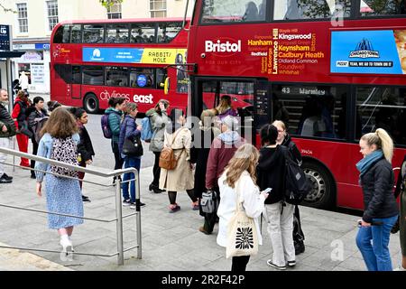 Autobus locali a due piani di colore rosso Bristol con persone in coda per salire a bordo l'un l'altro sul lato opposto della strada. Piazza del centro città, Regno Unito Foto Stock