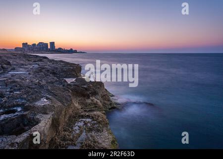 La donna siede sulle pietre fuori dalle mura della città di la Valletta e gode del tramonto Foto Stock