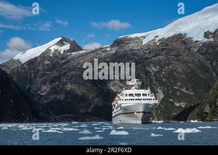 Mentre i passeggeri si godono il viaggio con un gommone Zodiac lungo il ghiacciaio, la nave da crociera della spedizione MS Bremen (Hapag-Lloyd Cruises) è surro Foto Stock