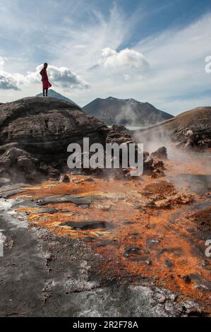 Un giovane uomo si erge sulle rocce e guarda il residuo arancione e le sorgenti calde vicino ad un vulcano attivo, Rabaul, Provincia Est della Nuova Gran Bretagna, Papua Nuova Guinea, S. Foto Stock