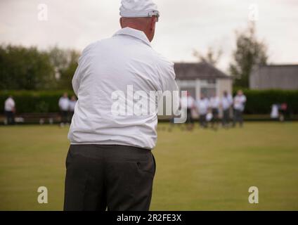 Un uomo calvo che indossa un cappello gioca a bocce di fronte a una folla fuori dal padiglione presso il Mauchline prato bowling verde a Mauchline; Ayrshire, Scozia, Regno Unito Foto Stock