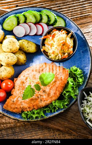 Cotoletta di maiale impanata ricoperta di pangrattato con patate e insalate di verdure Foto Stock