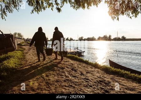 Il Delta del Danubio, una vecchia coppia, porta lo shopping lungo il sentiero lungo il fiume al sole serale, Mila 23, Tulcea, Romania. Foto Stock