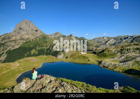 Donna mentre escursioni si siede su sperone di roccia e guarda Lac Roumassot e Pic du Midi d´Ossau, Lac Roumassot, Parco Nazionale dei Pirenei, Pirenei Atlantici, Foto Stock